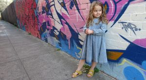 Little girl wearing Bobux shoes standing against wall