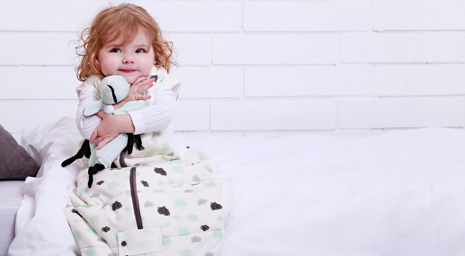 Baby sitting on bed holding ergoPouch Joey comforter