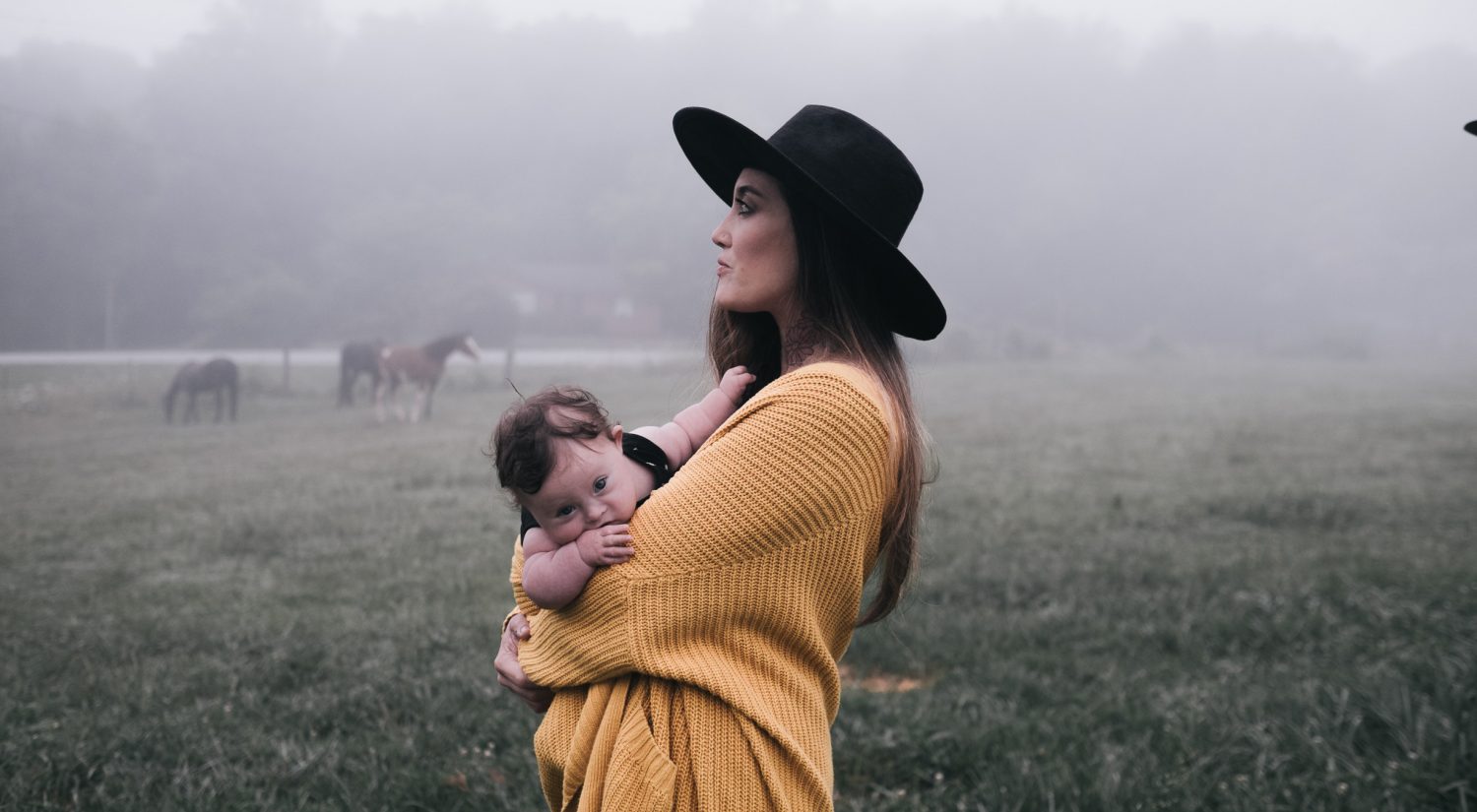 Mum holding baby with horses in the background